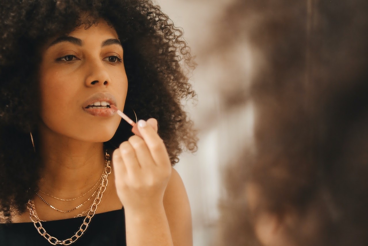 woman with necklace putting on lipstick