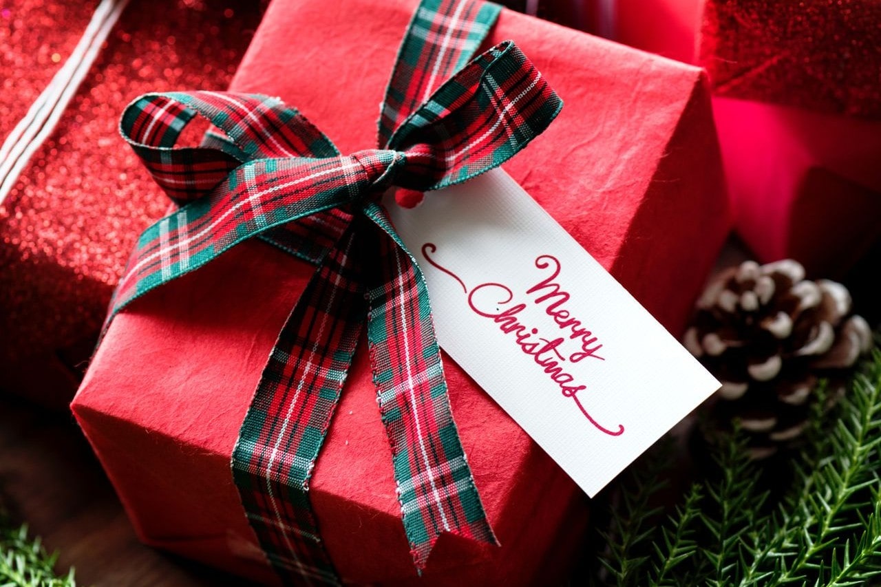 A small, red wrapped jewelry box lays in the middle of a pine wreath with a pinecone