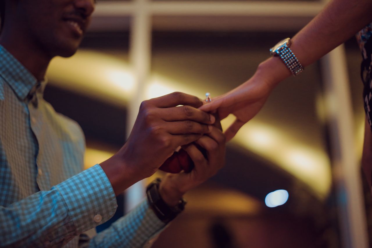 A close-up of a man putting a ring on a woman’s hand after proposing