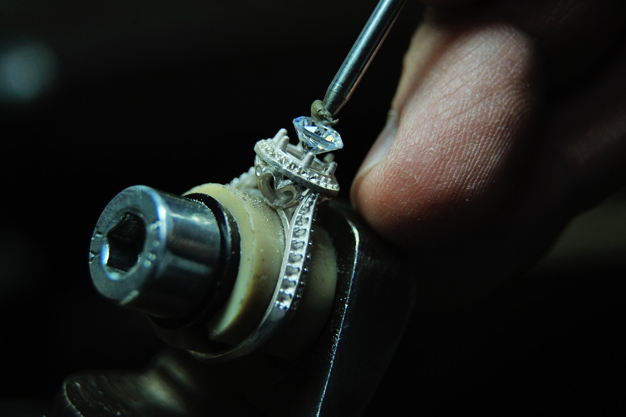 A jeweler sets a diamond into a halo engagement ring setting.