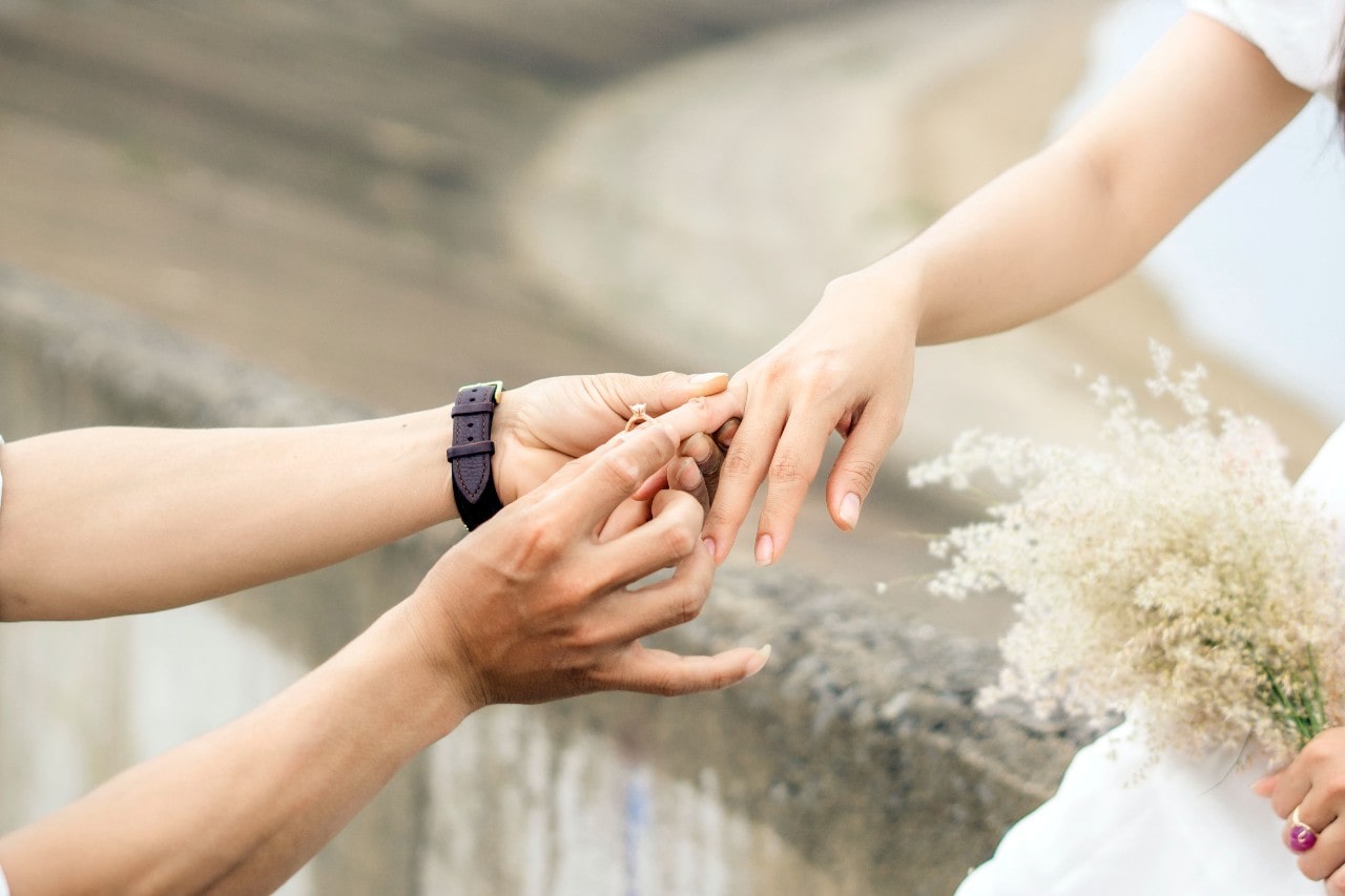 A person slips a gold engagement ring on a bride’s ring finger.