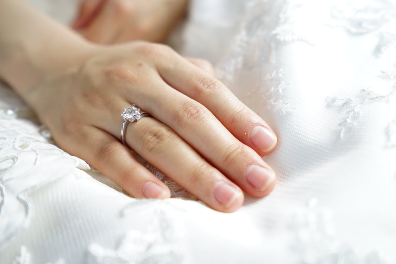 A close up of a woman&rsquo;s hand with white gold diamond engagement ring on a white fabric