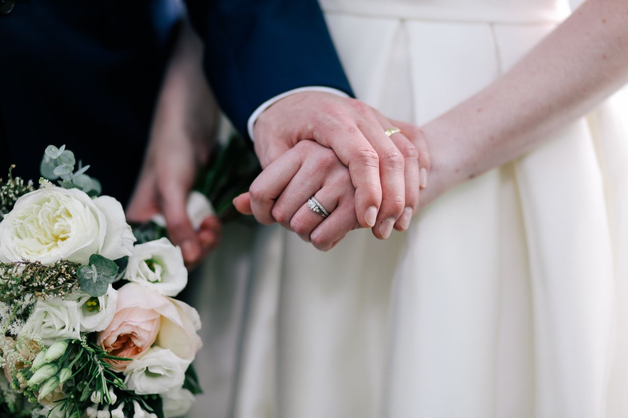 A close-up of a bride and groom holding hands, with emphasis on their wedding bands.