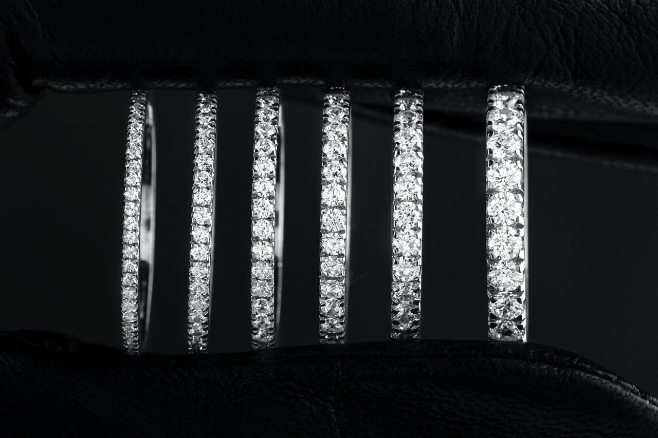 A close-up of six diamond wedding bands lined up vertically, showcasing sparkling gemstones set in metal bands, against a black background.
