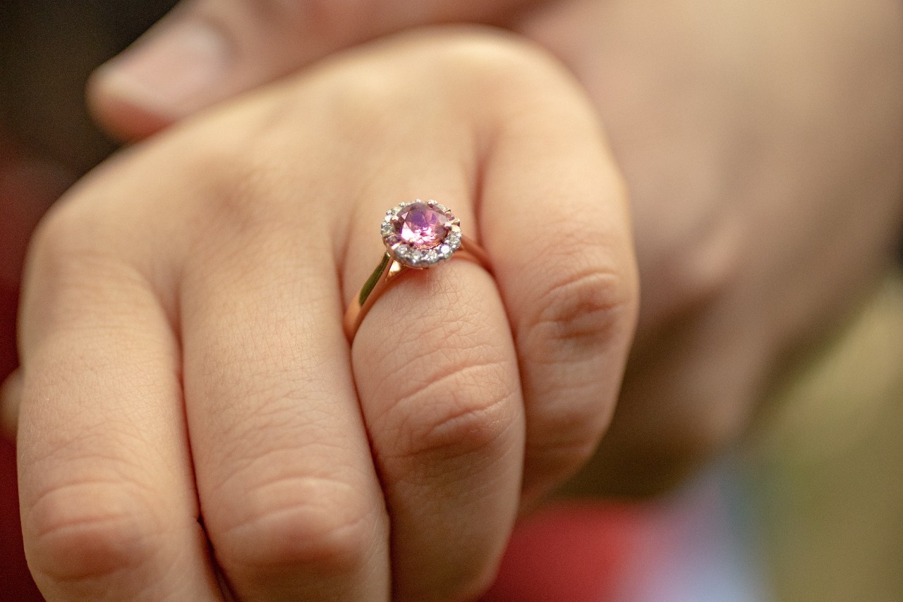 a woman’s hand a rose gold halo engagement ring featuring a purple center stone