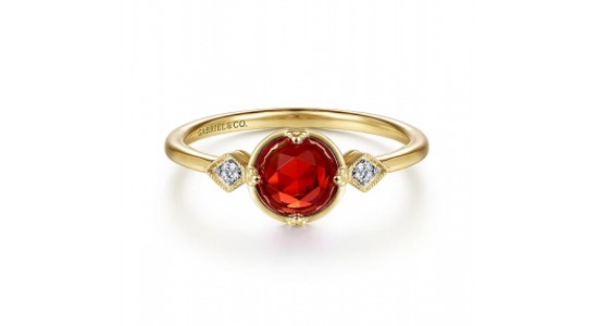 a yellow gold ring featuring a round cut red garnet and two diamond accent stones