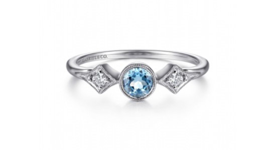 a white gold ring featuring a bezel set, round cut blue topaz and diamond accent stones