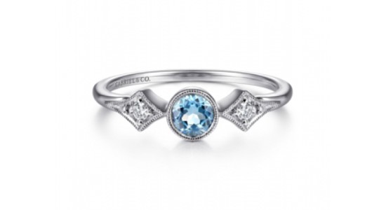 a white gold ring featuring a bezel set, round cut blue topaz and diamond accent stones