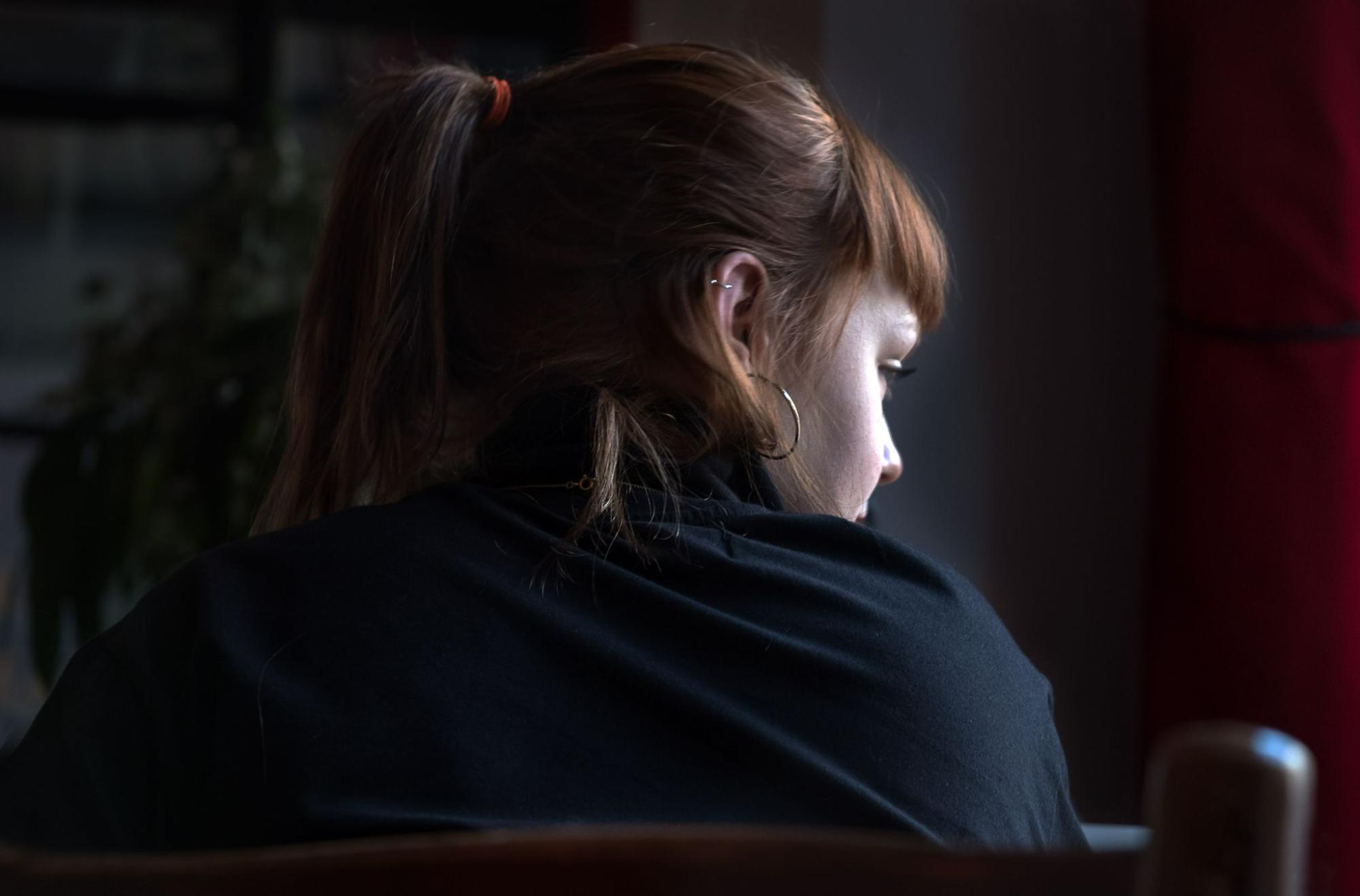 a woman wearing a ponytail and hoop earrings looks out the window.