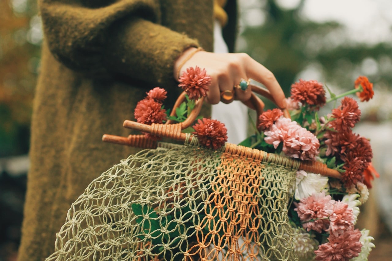 a person in a green sweater holding a bag of flowers and wearing a gemstone fashion ring