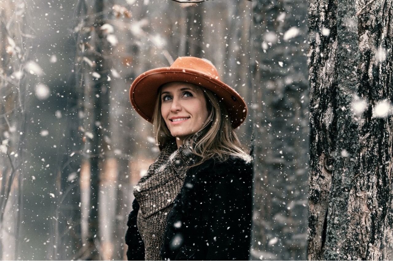 A woman bundled up in warm clothes walks through a snowy forest in the winter.