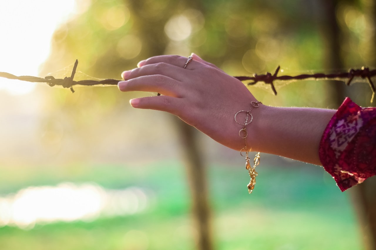 A woman reaching out to barbed wire, a gold bracelet dangling from her wrist.