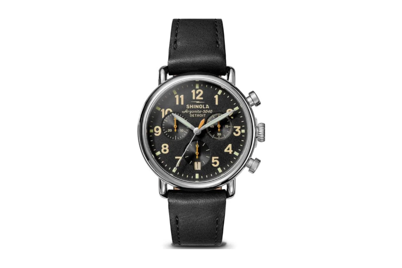 A Shinola watch with a black leather strap, a silver bezel, and a black dial with three black subdials, and cream numbers.