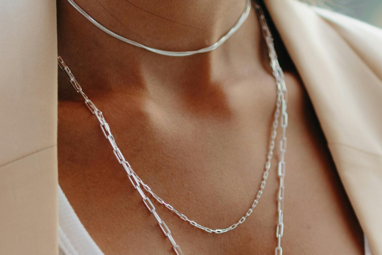 A close-up of a woman&rsquo;s decolletage and neckline adorned with three delicate, layered chain necklaces.