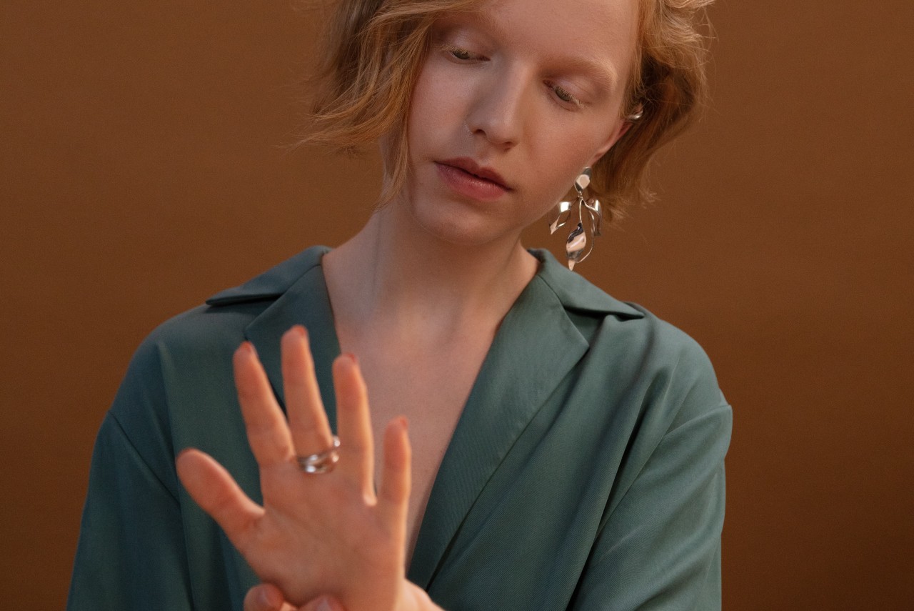 A photo of a young woman wearing a green blouse and an ornate gold earring, admiring a gold ring on her finger.