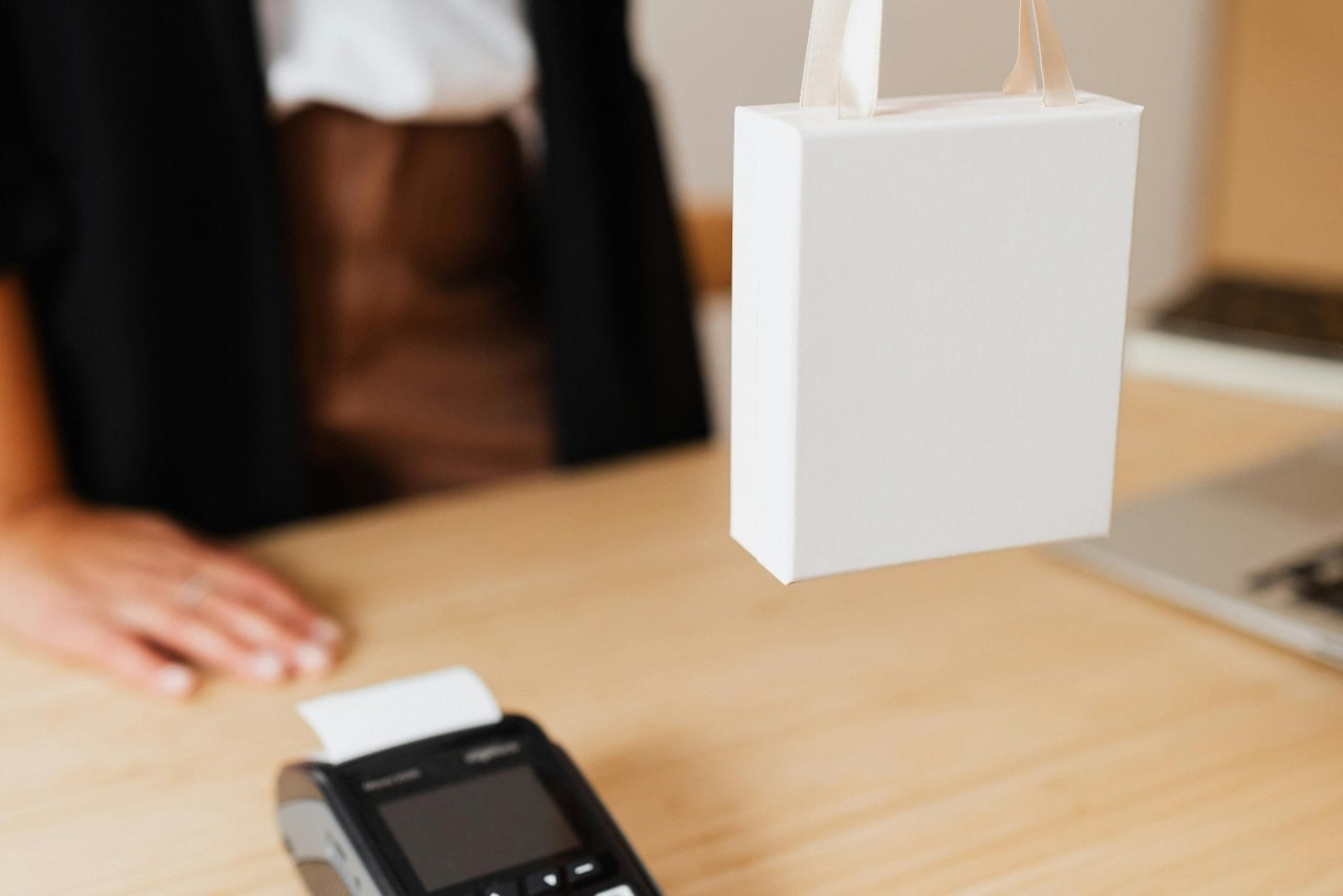A close-up of a jeweler giving a small white shopping bag to a customer out-of-frame as they complete their purchase.