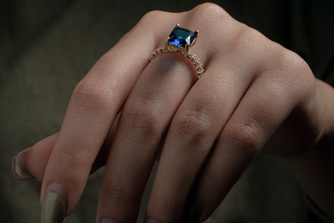 close up image of a hand wearing a sapphire gold ring with diamond accents