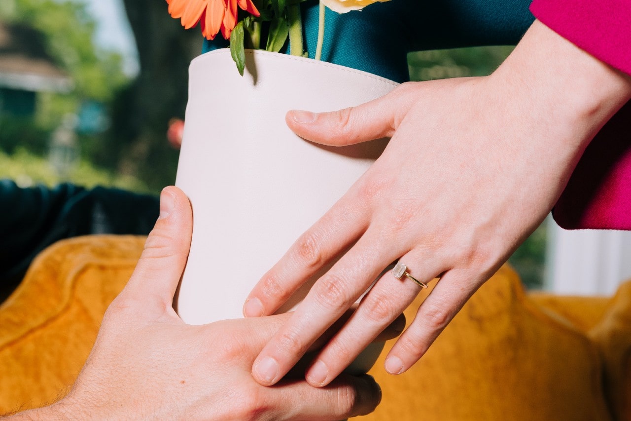 a couple passing a flower pot, the woman’s hand donning a yellow gold engagement ring