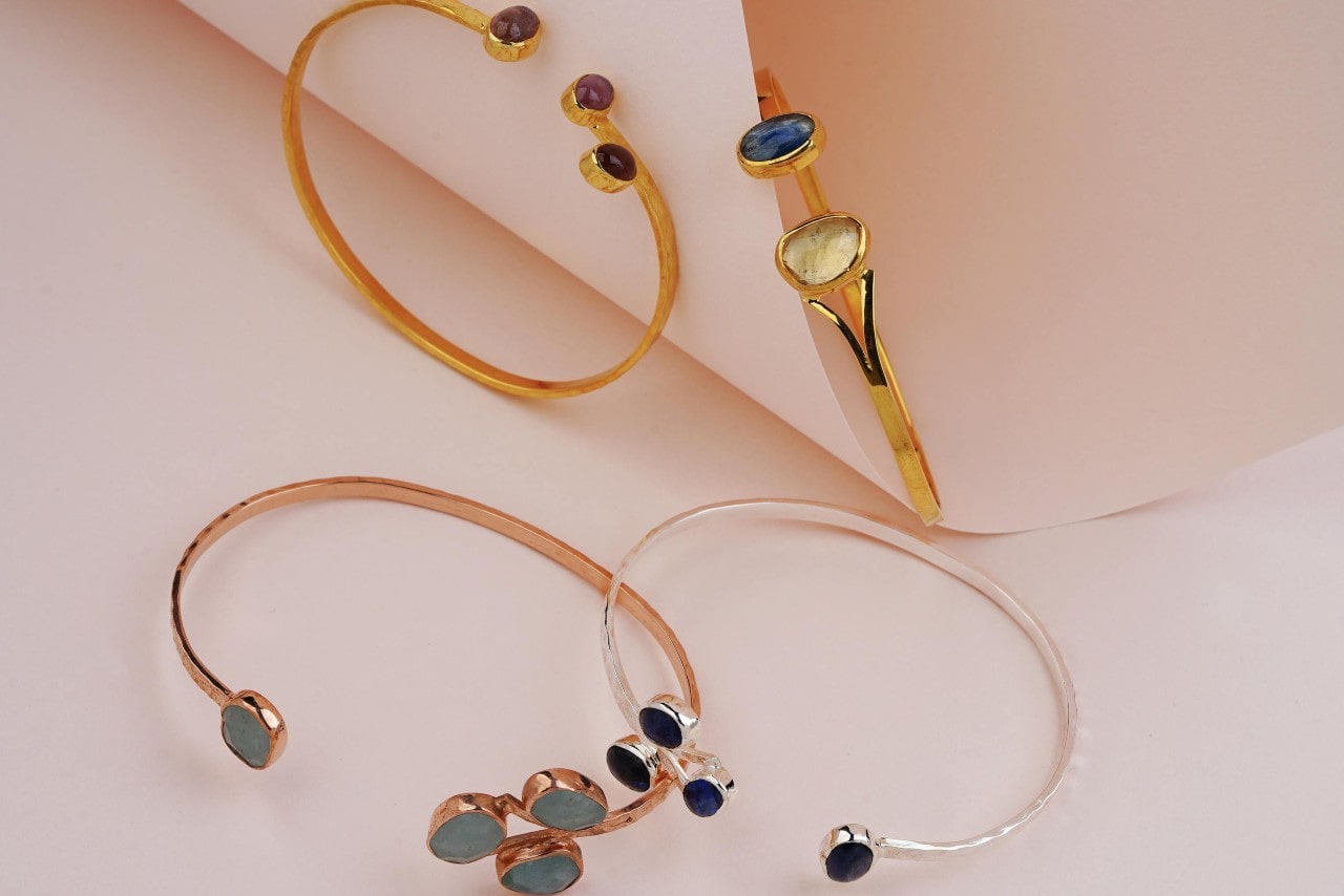four cuff bracelets with different colored gemstones on a white surface