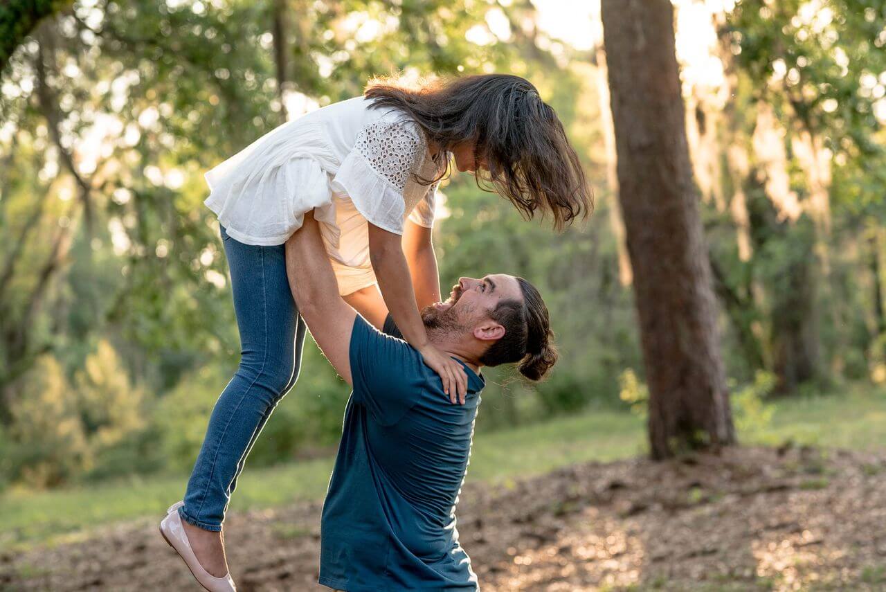 A father holds a daughter in his hands in front of a forestry background.