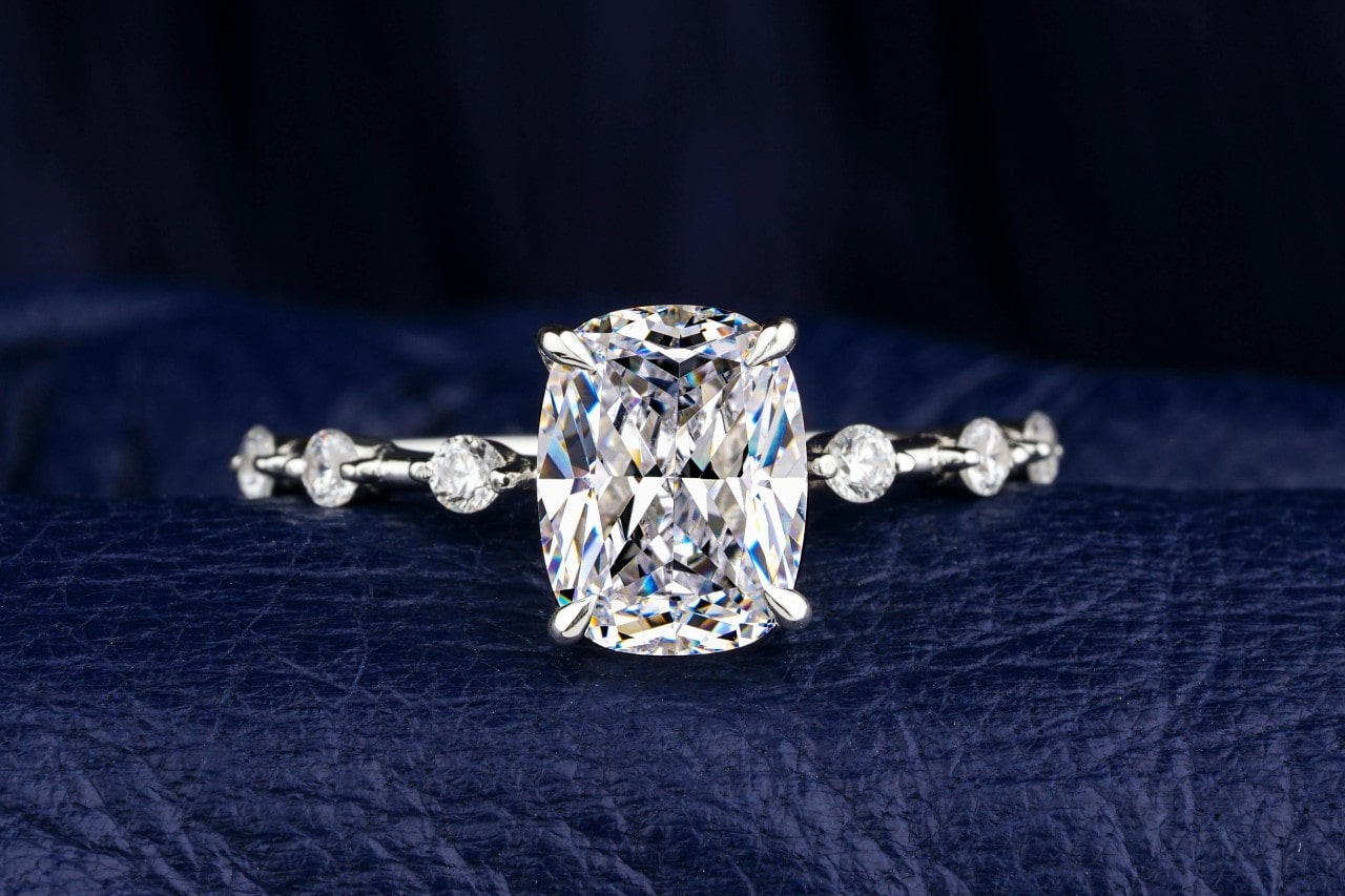 close up image of a diamond engagement ring with evenly spaced side stones on a leather surface