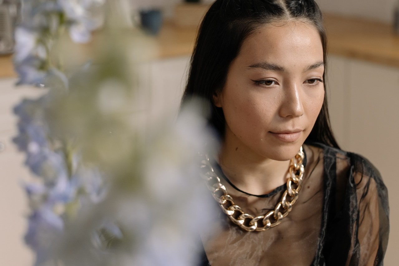 a woman wearing a large, chunky gold necklace with a blurred out flower in the foreground