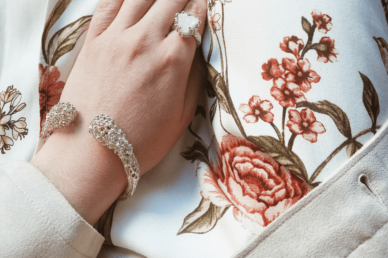 a woman’s hand in her lap, wearing a cuff bracelet and a bold ring