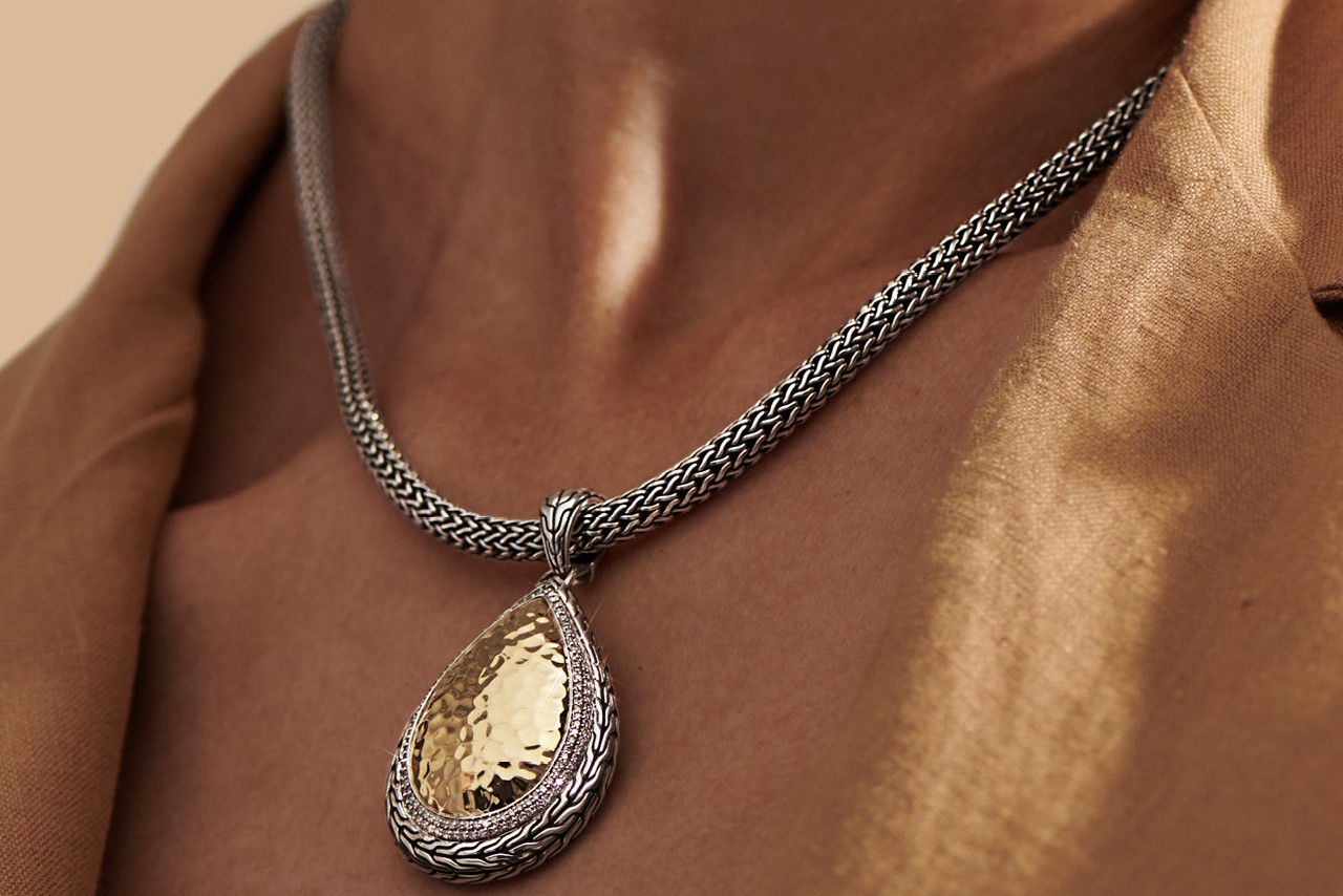 Woman wearing a hammered gold pendant and woven chain necklace by John Hardy