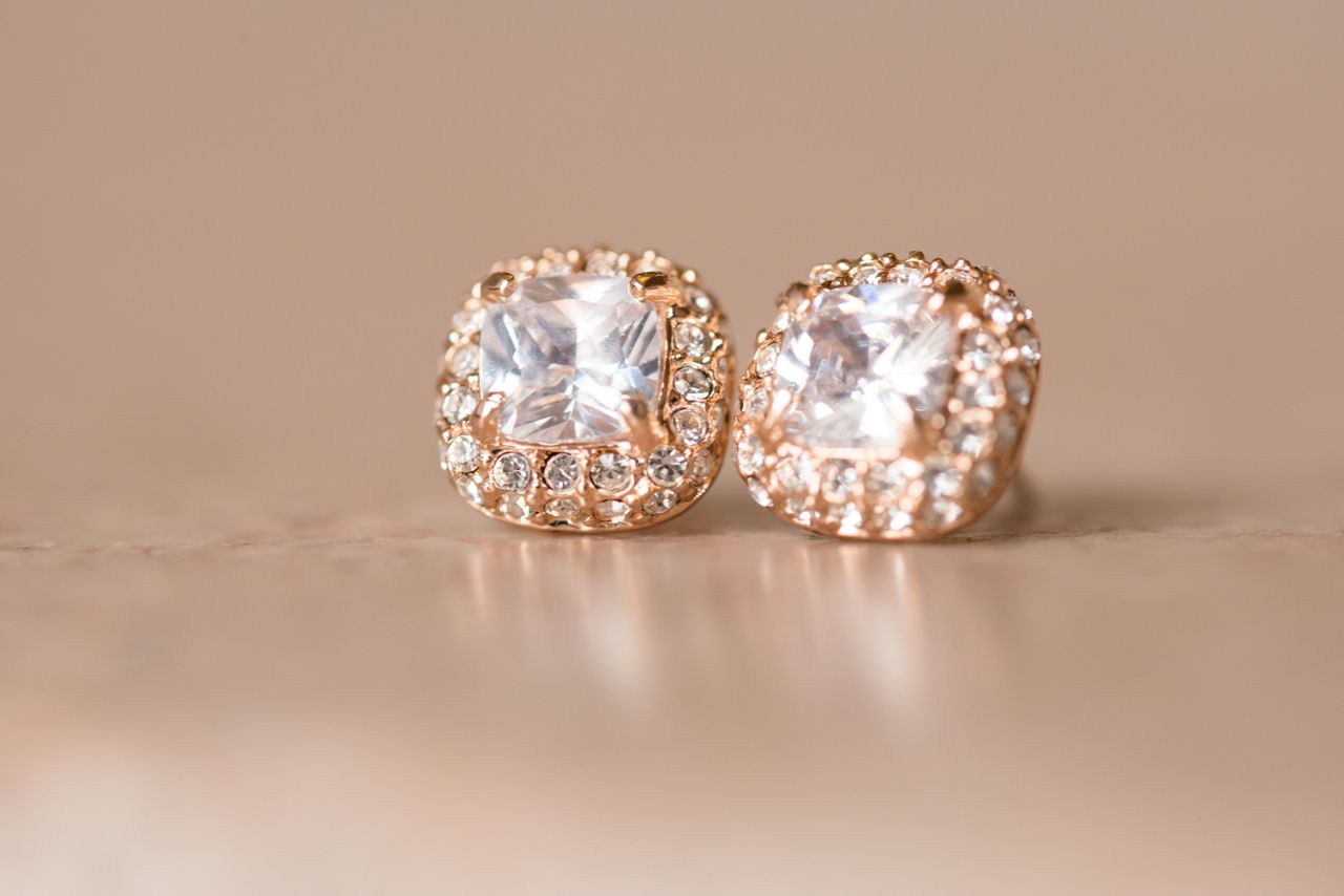 Cushion-cut diamond stud earrings set in rose gold on a soft beige surface. Cushion-cut diamond stud earrings set in rose gold on a soft beige surface.