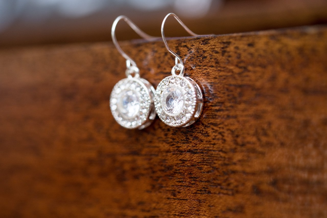 A pair of round diamond drop earrings with pavé settings, hanging from a polished wooden surface A pair of round diamond drop earrings with pavé settings, hanging from a polished wooden surface