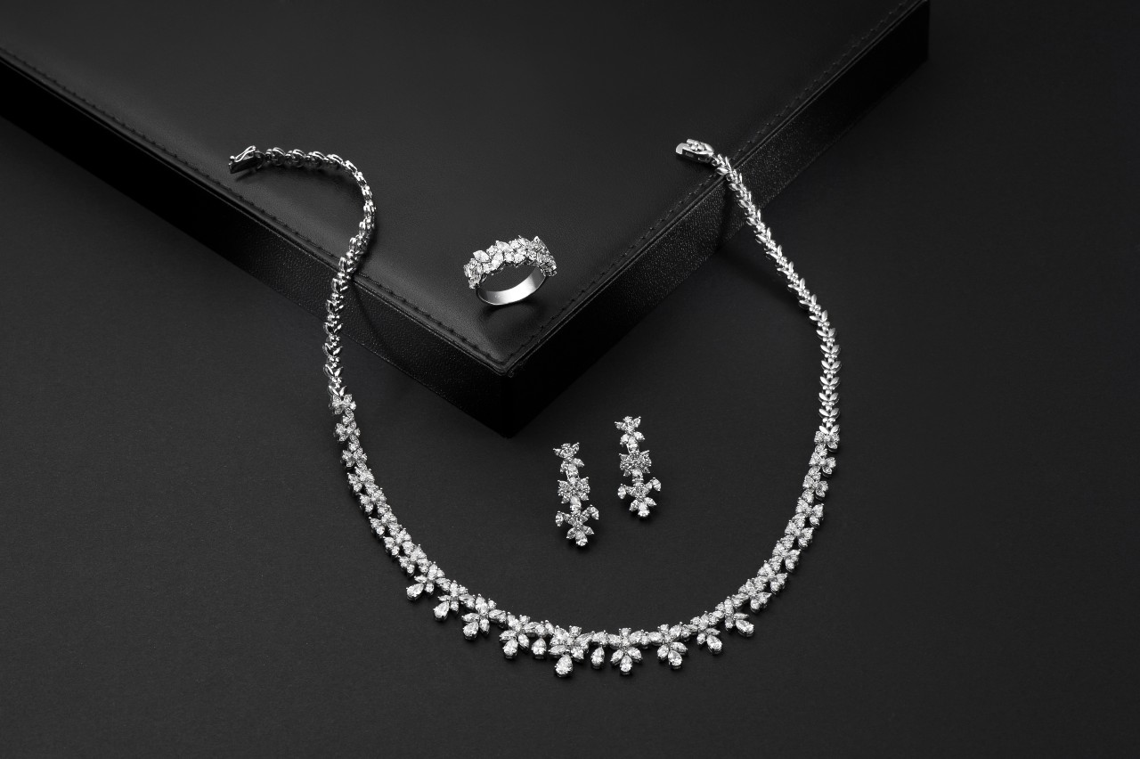 A diamond jewelry set with a necklace, earrings, and ring displayed on a dark surface.