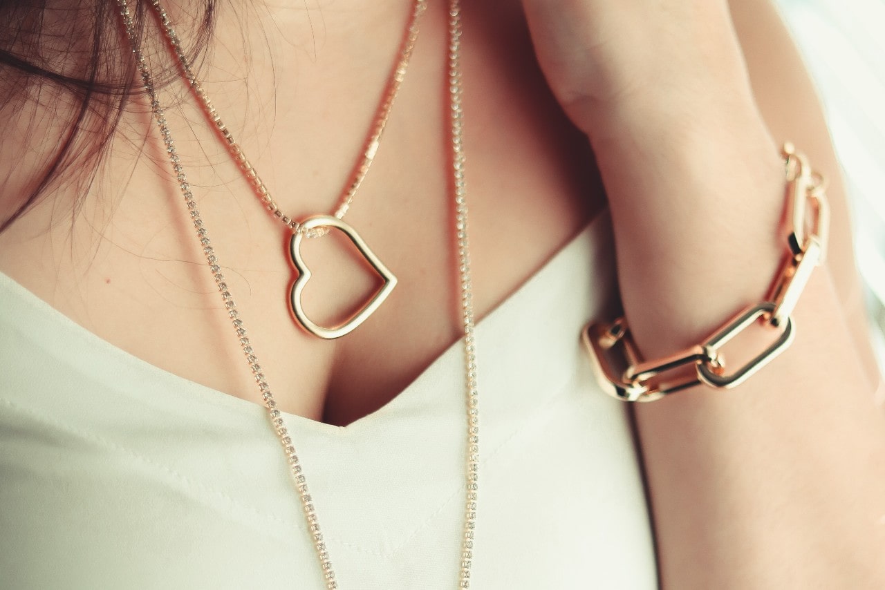 a lady’s neckline and arm wearing fine necklaces and a bracelet 