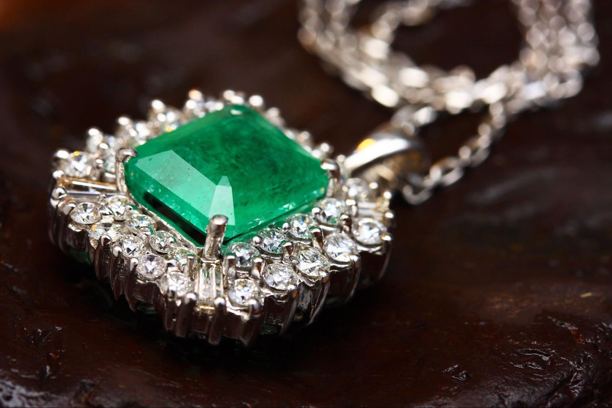 A large emerald diamond necklace pendant laying on a dark wood surface and sparkling in the light.