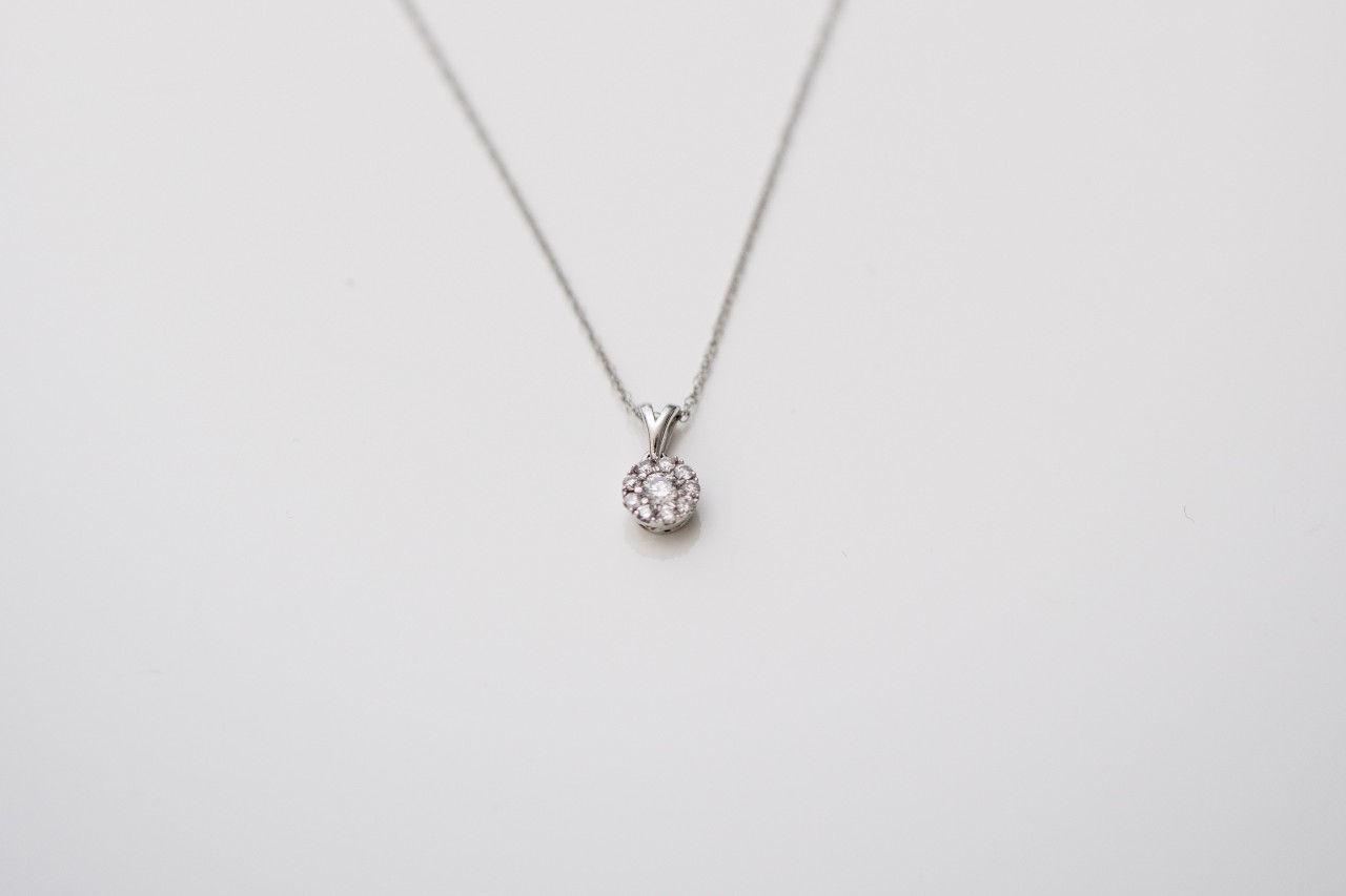 A close-up of a diamond pendant necklace laying on a plain white surface.