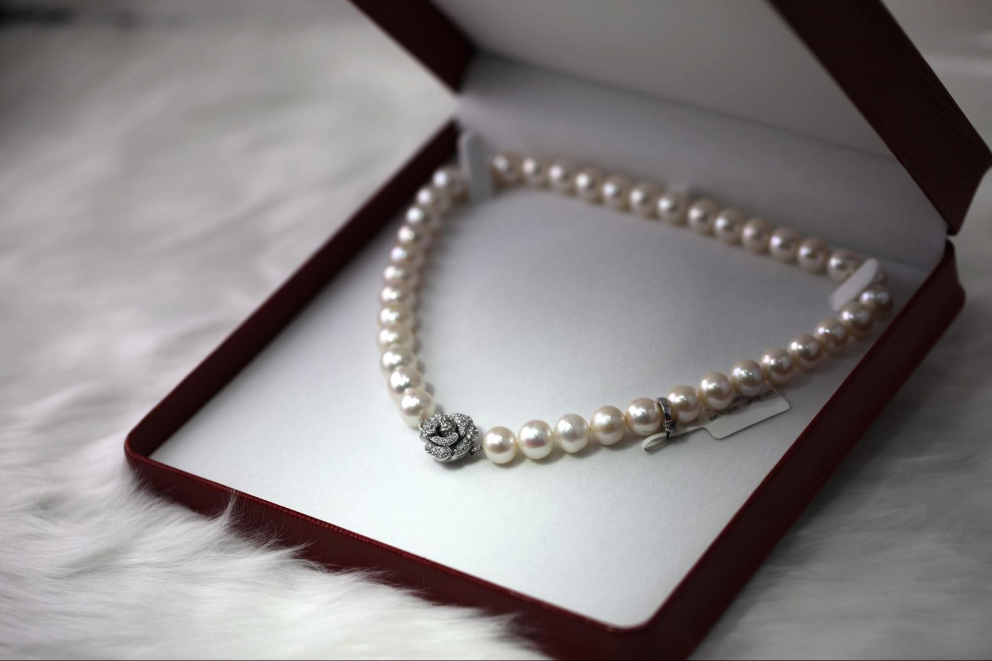 A pearl necklace with a diamond floral centerpiece displayed in an open jewelry box on white fur.