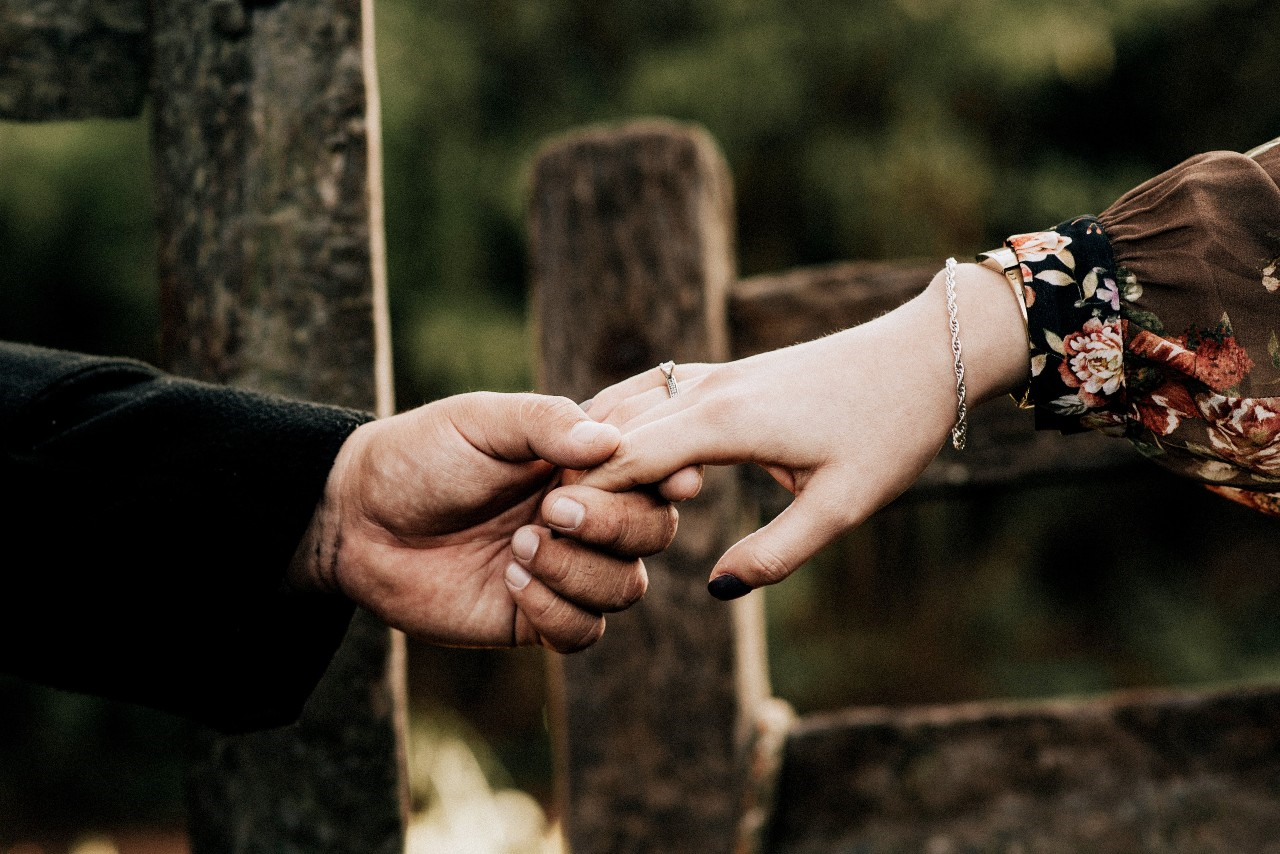 A closeup of a woman holding hands with her partner by a rustic fence.