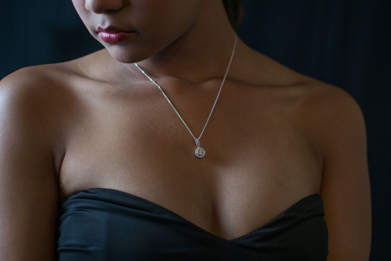 A woman in a black dress wears a solitaire diamond necklace.