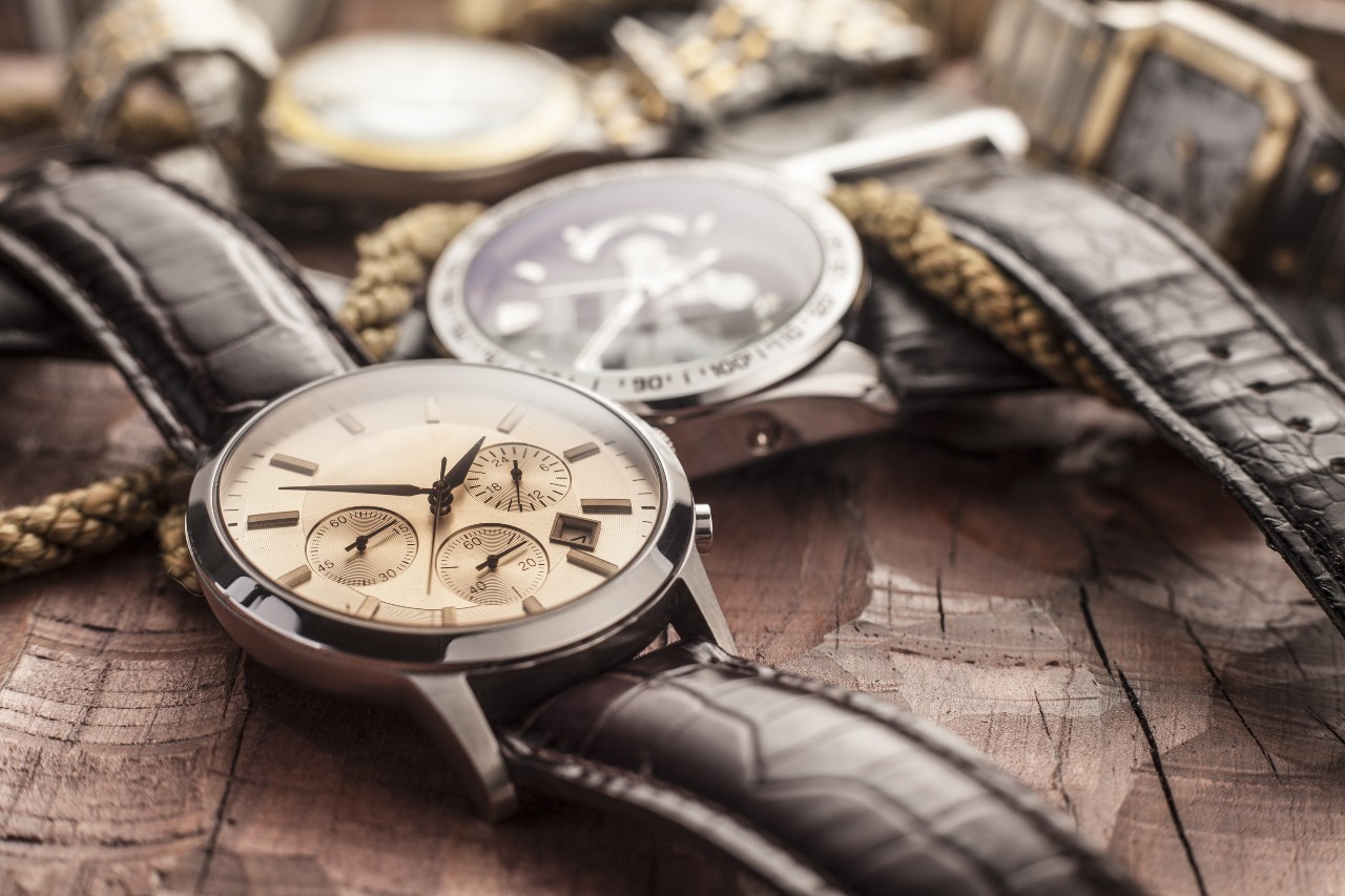 Close-up of two wristwatches with brown leather straps on a rustic wooden surface.
