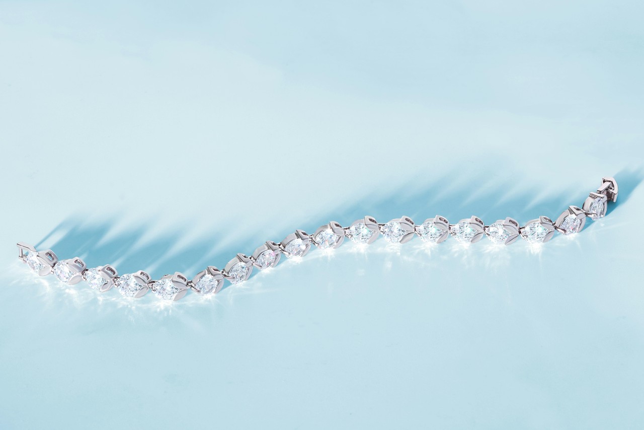 A white gold round cut diamond tennis bracelets on a light blue surface. A white gold round cut diamond tennis bracelets on a light blue surface.