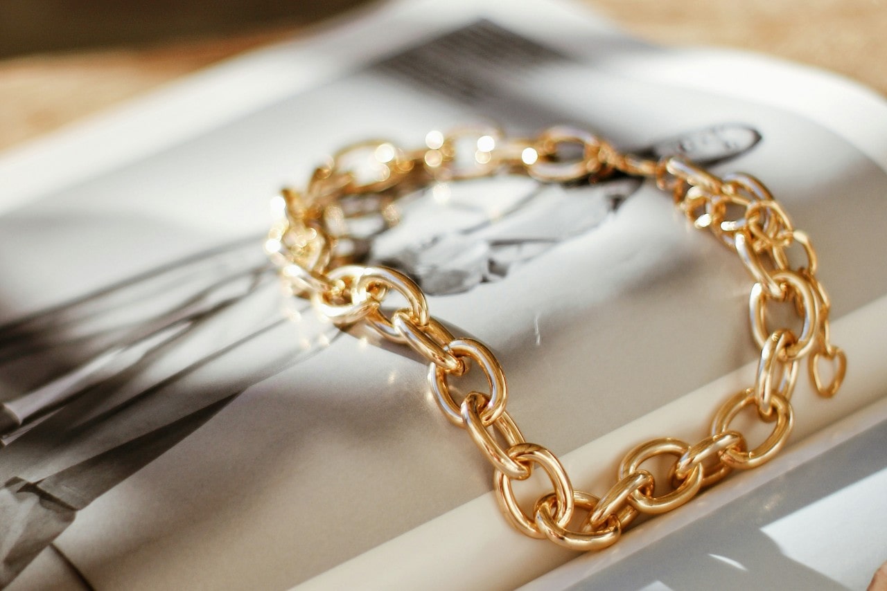 A yellow god chain bracelet across a book with photographs A yellow god chain bracelet across a book with photographs