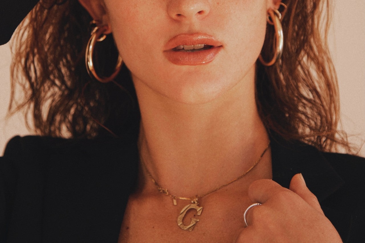 Woman with a yellow gold initial pendant, white gold ring, and yellow gold hoop earrings Woman with a yellow gold initial pendant, white gold ring, and yellow gold hoop earrings